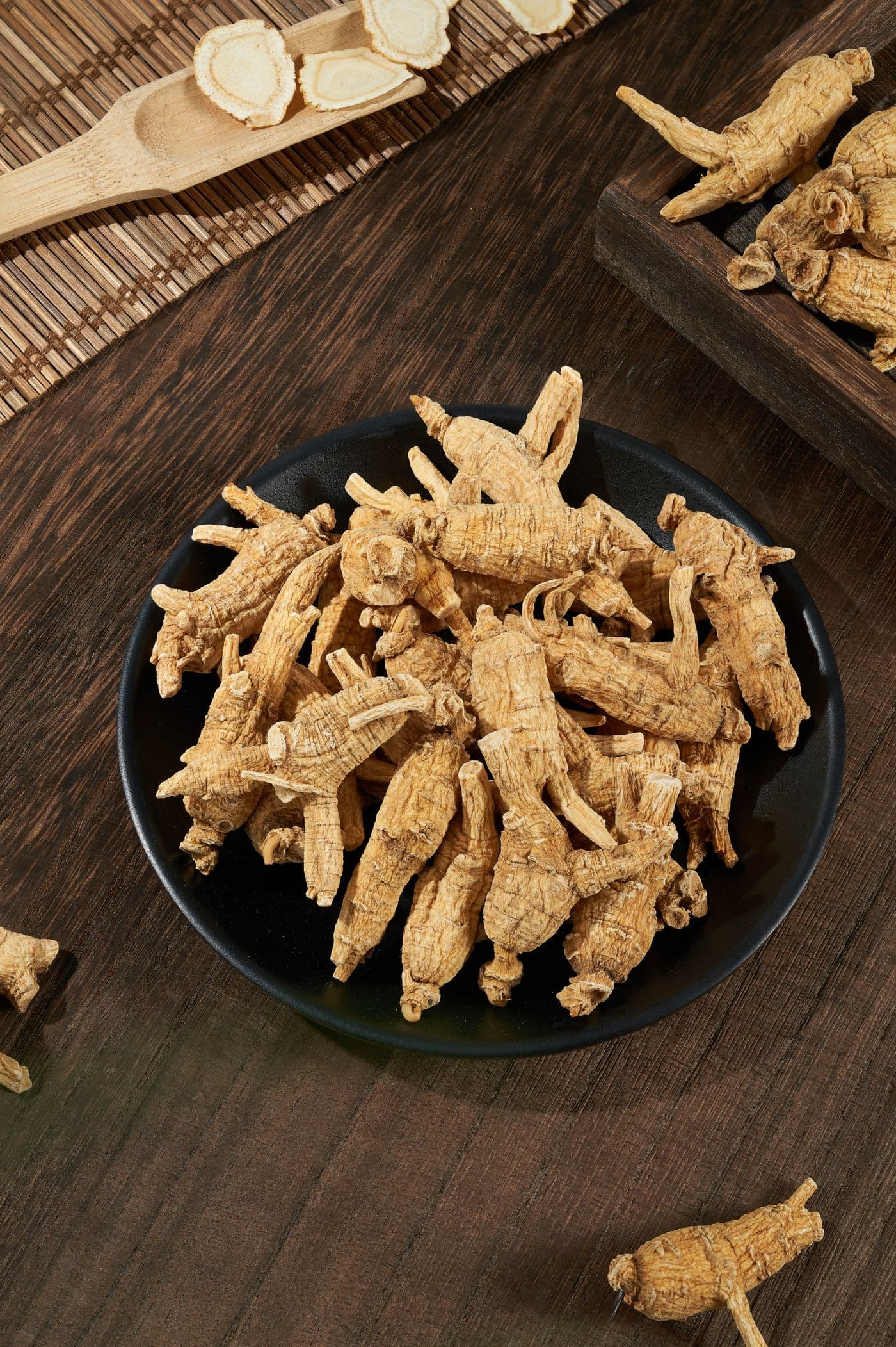 Whole dried ginseng roots in a black dish on a dark wooden table