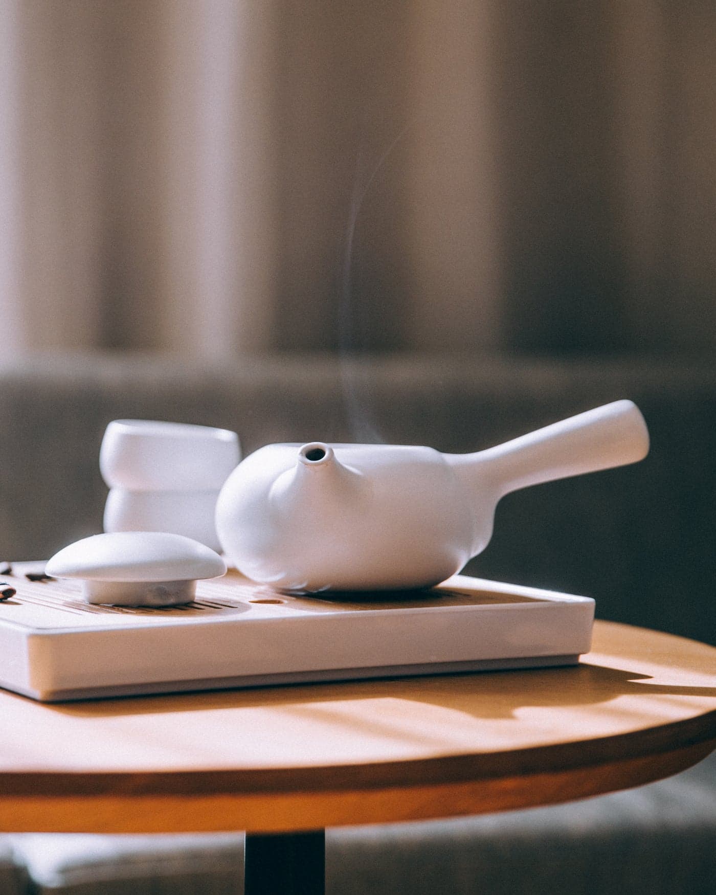 A white ceramic tea set — pot, cups and tray — on a sunlit table